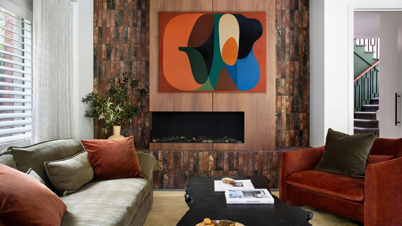 modern living room with brick fireplace feature wall, brightly colored artwork, sage green sofa with orange cushions, a red velvet armchair with olive green cushion and black coffee table