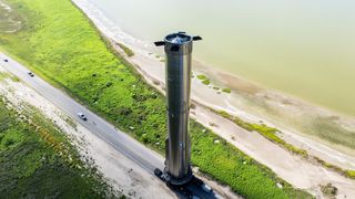 aerial shot of a big silver rocket rolling along a seaside road