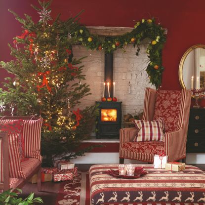 A red living room decorated for Christmas with a tall Christmas tree and a garland around an alcove for a wood-burning stove