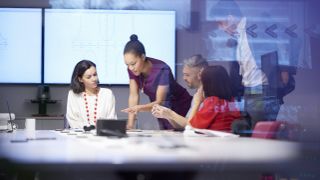 IT leaders discussing digital transformation plans and technical debt issues in an office environment while looking at statistics on a laptop.