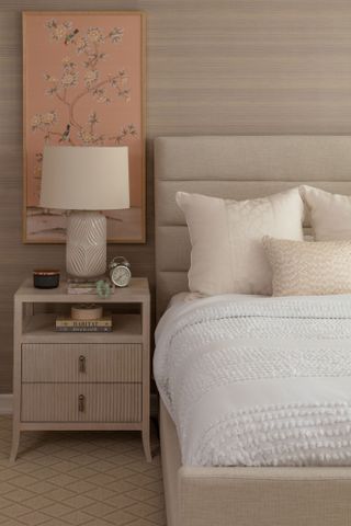 bedhead with chinoiserie framed print neutral walls and floors and white bedlinen with bedside table and lamp