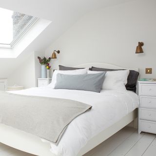 White loft bedroom with skylight, wall lights and wooden floor