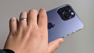En mobiltelefon av typen iPhone 14 Pro Max holdt i en hånd.