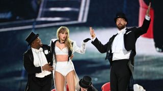 From left to right: Kam Saunders smiling and holding up Taylor Swift, she's looking at Travis Kelce who is standing with his arms in the air during The Eras Tour in London on June 23, 2024.