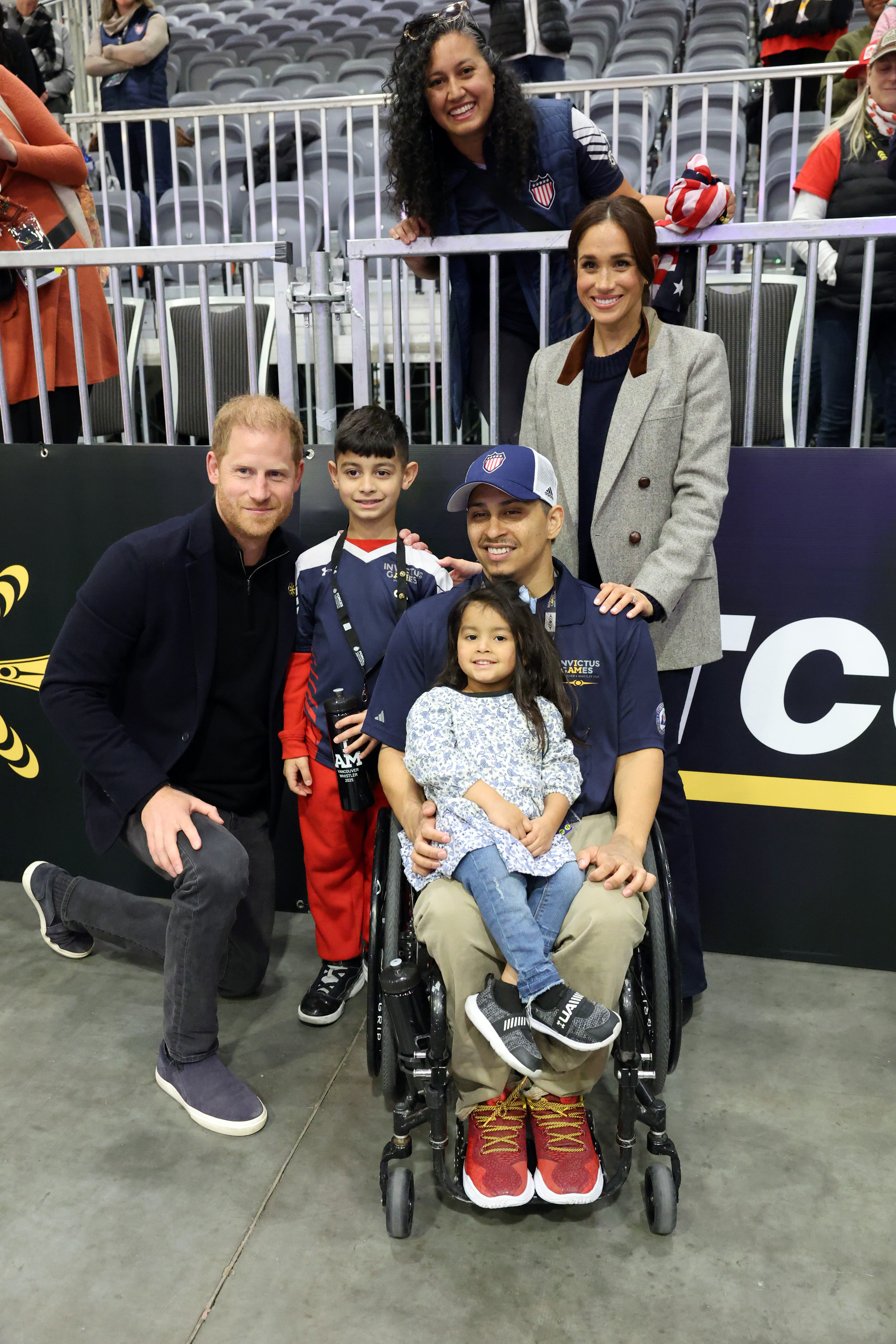 Prince Harry and Meghan Markle posing with a man in a wheelchair and two children