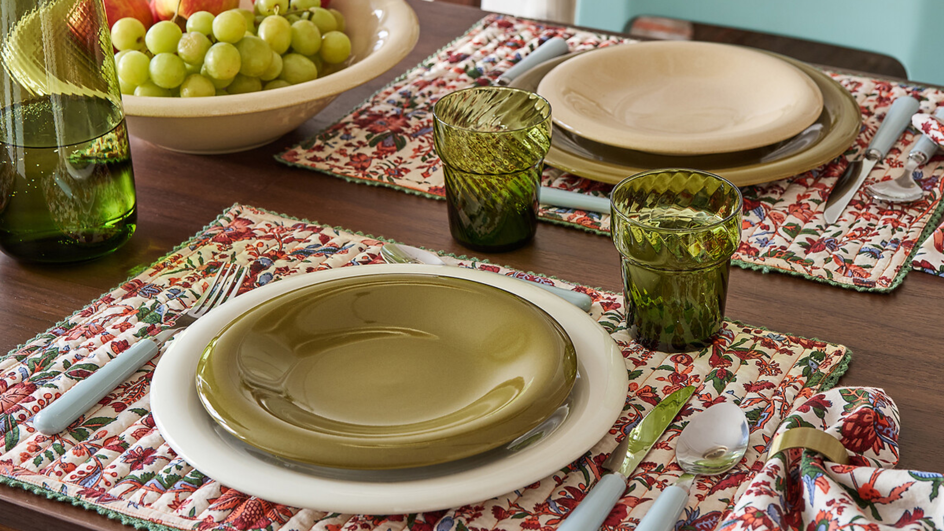 Close-up image of a color table setting with patterned, quilted placemats. There are double stacked bubble plates at the setting in olive green, white, and tan.