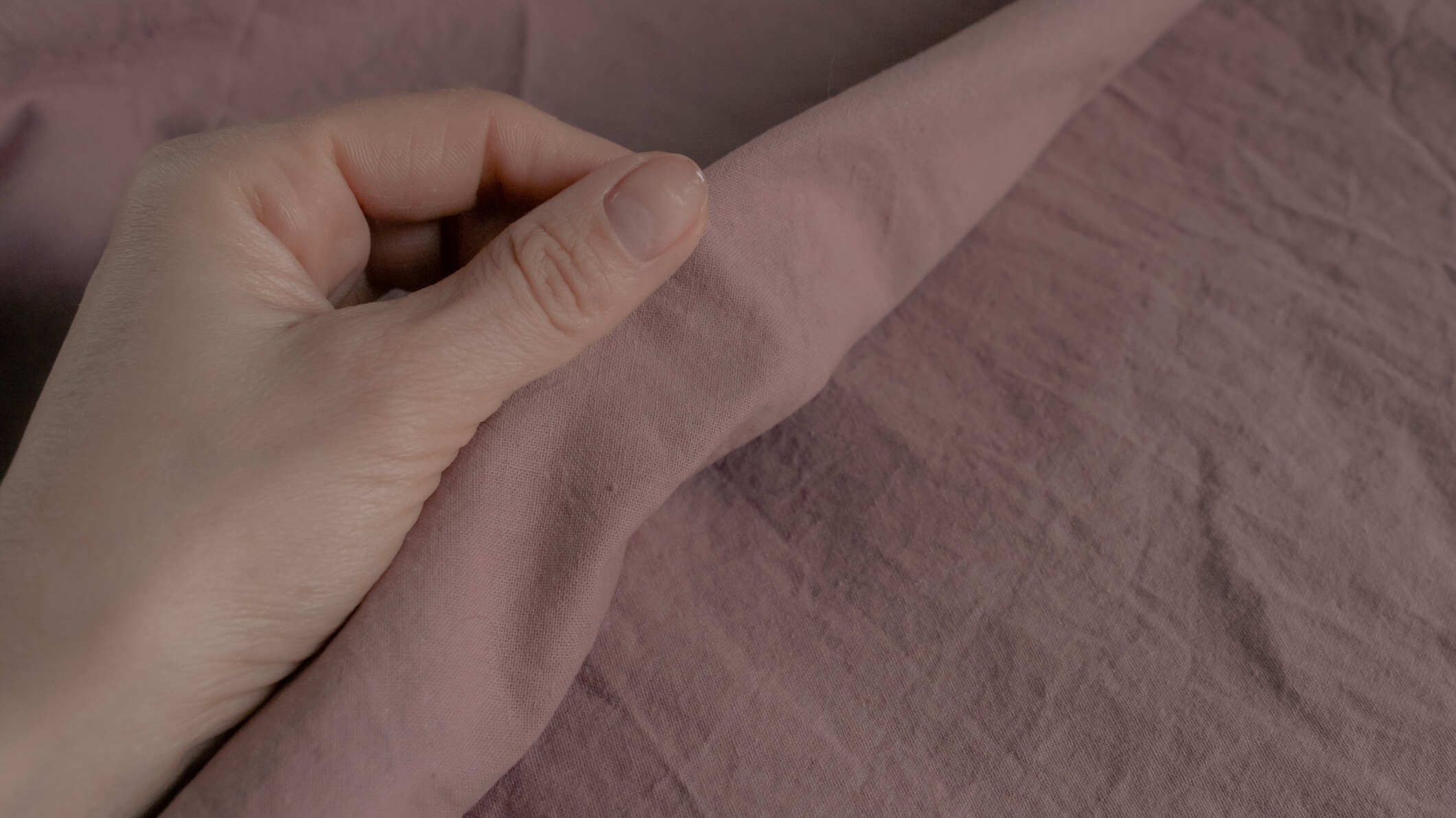 Hand assessing a pink bed sheet a close-up shot