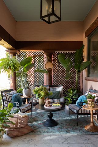 An outdoor balcony space with easy chairs, a carpet and tall leafy plants