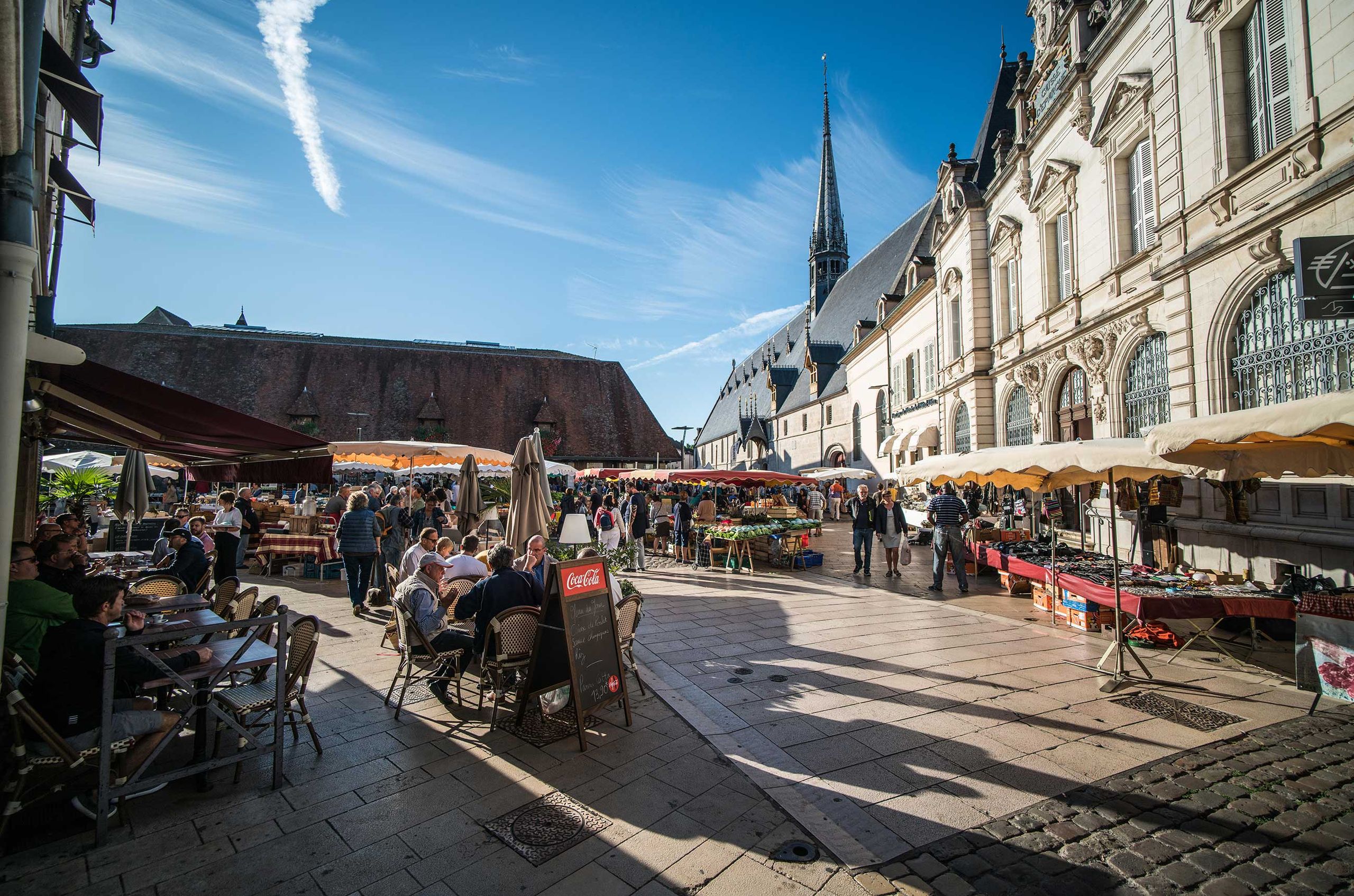 People sitting at outdoor cafe tables and shopping at the stalls in a produce market in Burgundy