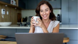 woman smiling at laptop screen holding cup of coffee