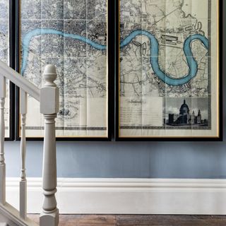 A blue-painted hallway with a staircase and a large-scale framed London map hanging on the wall