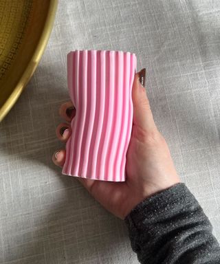 A woman's hand with brown painted nails holding a pink damp duster, agsinst a white fabric background