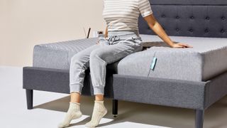 A woman tests the edge support of her new Siena Mattress by sitting on its edges.