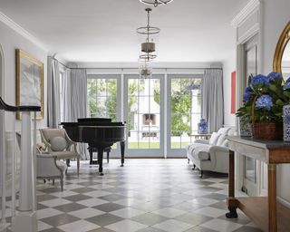 An entrance hall with grey and white checkboard floor, grand piano and entry to blue dining room