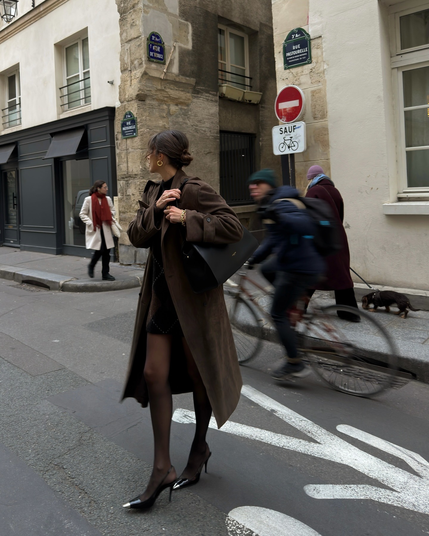 French influencer @juliesfi walks down the streets of Paris wearing a dark brown trench coat with tights and slingback heels.