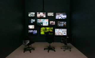 Exhibition view of Possessed featuring lit surveillance screens