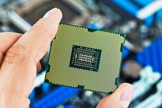 Macro view of modern multicore CPU processor in human hand with PC computer motherboard in background