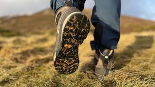 A pair of feet wearing Scarpa Mescalito TRK Pro GTX hiking boots, walking away from the camera with the sole of the boot visible