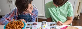 Two children sit side by side reading a copy of The Week Junior