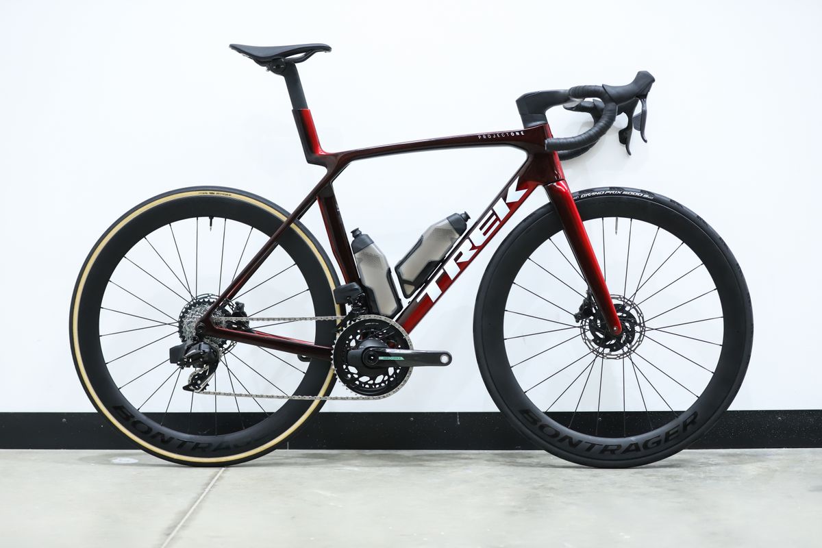 A red Trek Madone SLR 7 (gen 8) stands against a white wall