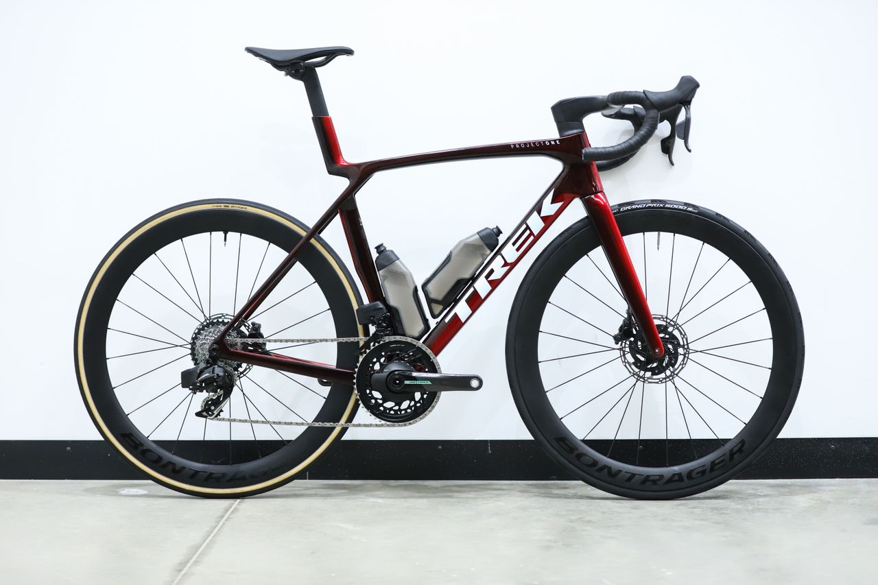 A red Trek Madone SLR 7 (gen 8) stands against a white wall