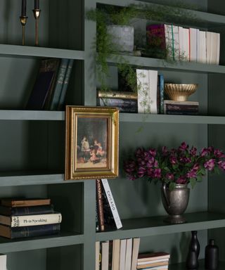 An up-close shot of green bookshelves with art hanging and vintage trinkets amongst books
