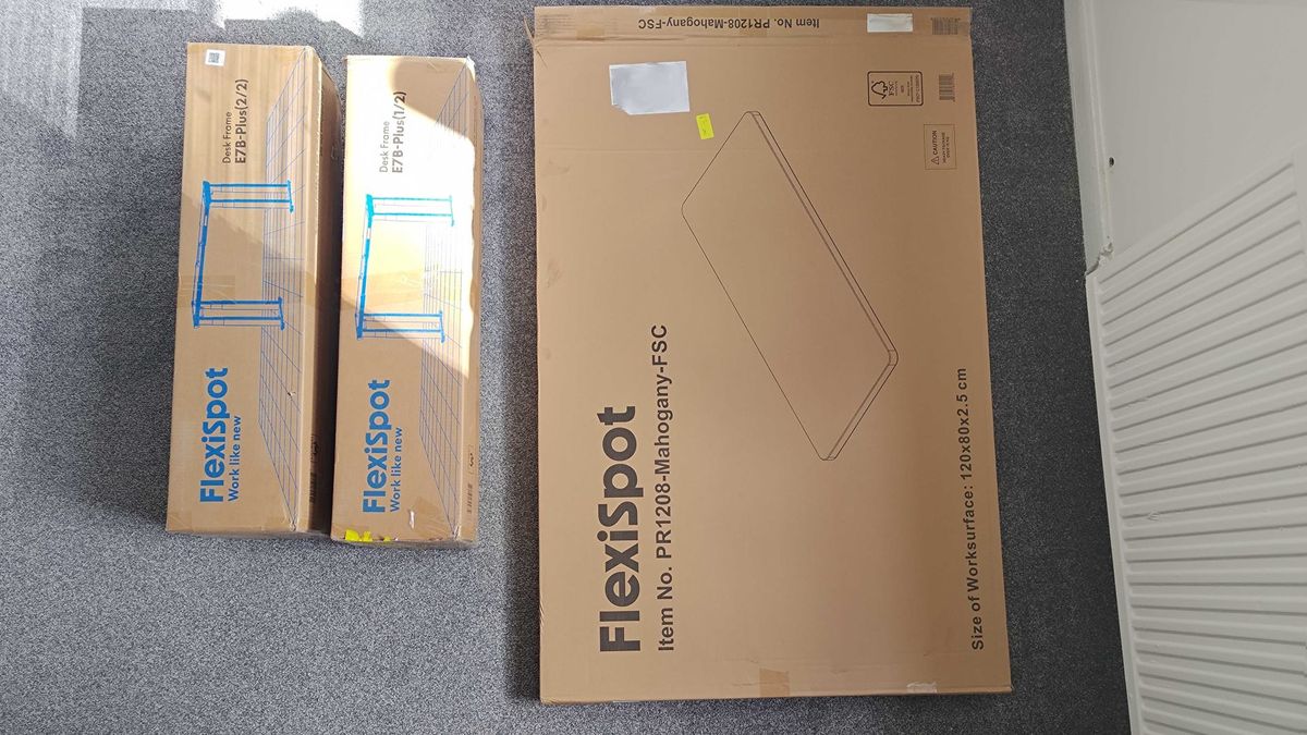 Flexispot E7 Plus boxes with two for legs and mechanism and one for the gaming desk top on grey carpet