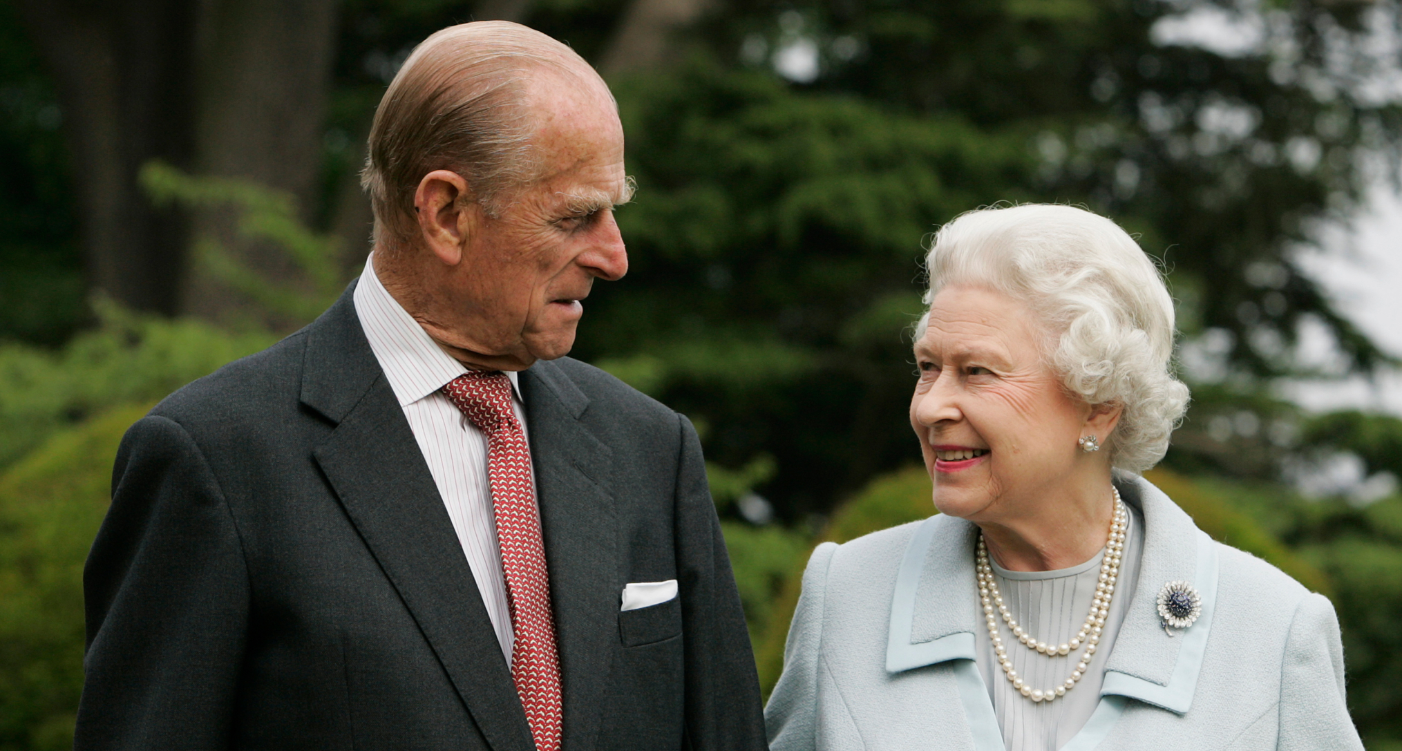 Queen Elizabeth and Prince Philip smiling at each other in front of trees