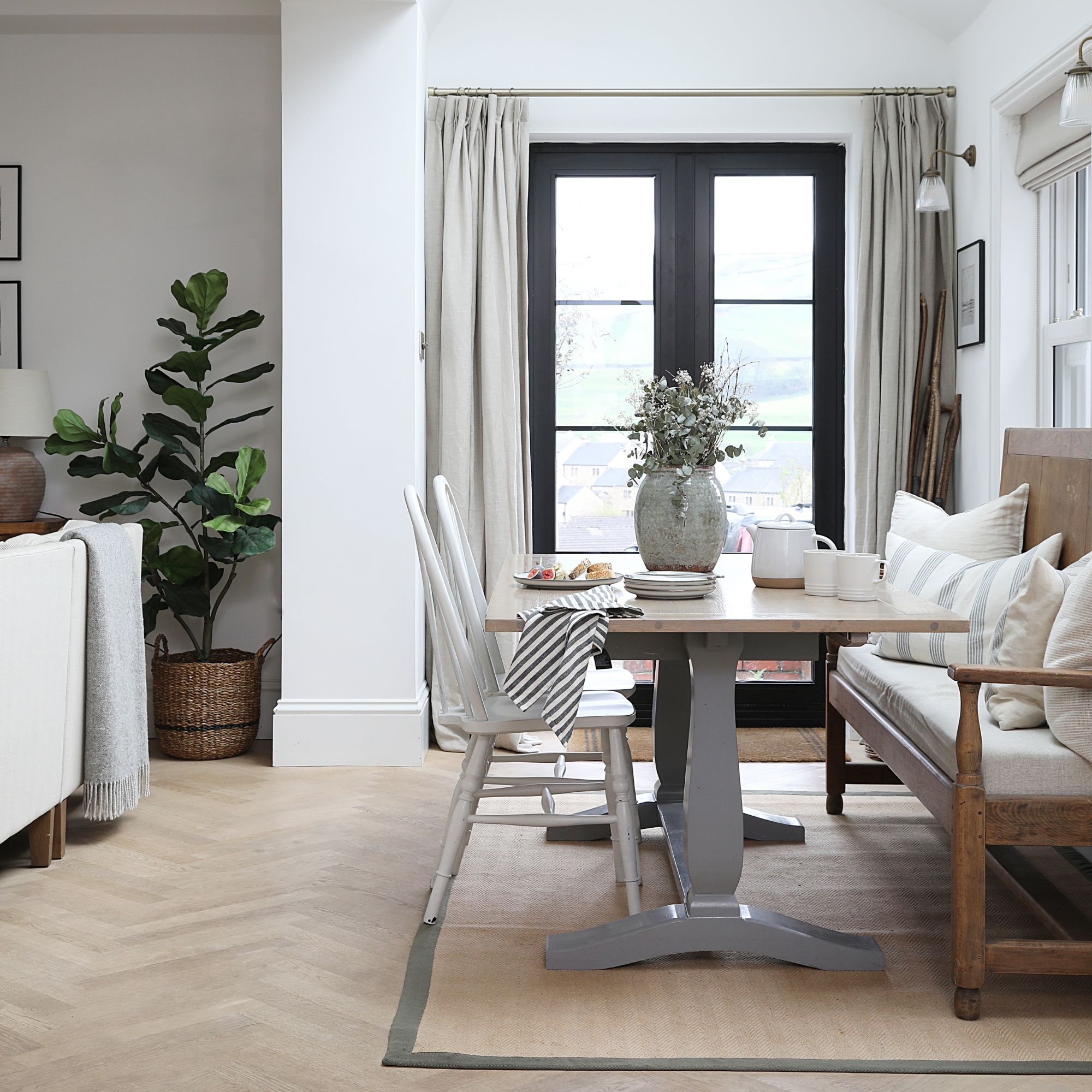 An open-plan dining area connected to the living room in a muted, neutral colour palette with a rectangular wooden table, white chairs and an upholstered bench