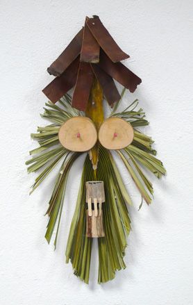 Masquerade-like mask created using wood and palm trees, hanging from a wall