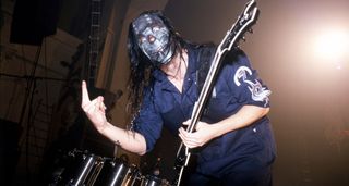 Mick Thomson of Slipknot is masked and wearing a blue boiler suit as he throws the horns live onstage during the Iowa metal institution's debut UK tour.