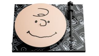 Pro-Ject Peanuts turntable on a white background. The platter has a large Charlie Brown face on it and the body of the turntable has black and white frames from Peanuts cartoons.