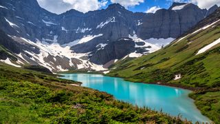 A view of a blue lake at the foot of a snowy mountain range