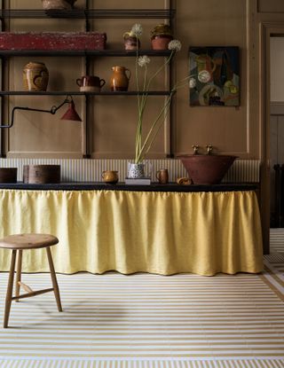 A kitchen with a yellow sink skirt and a taupe and white striped tile layout on the floor