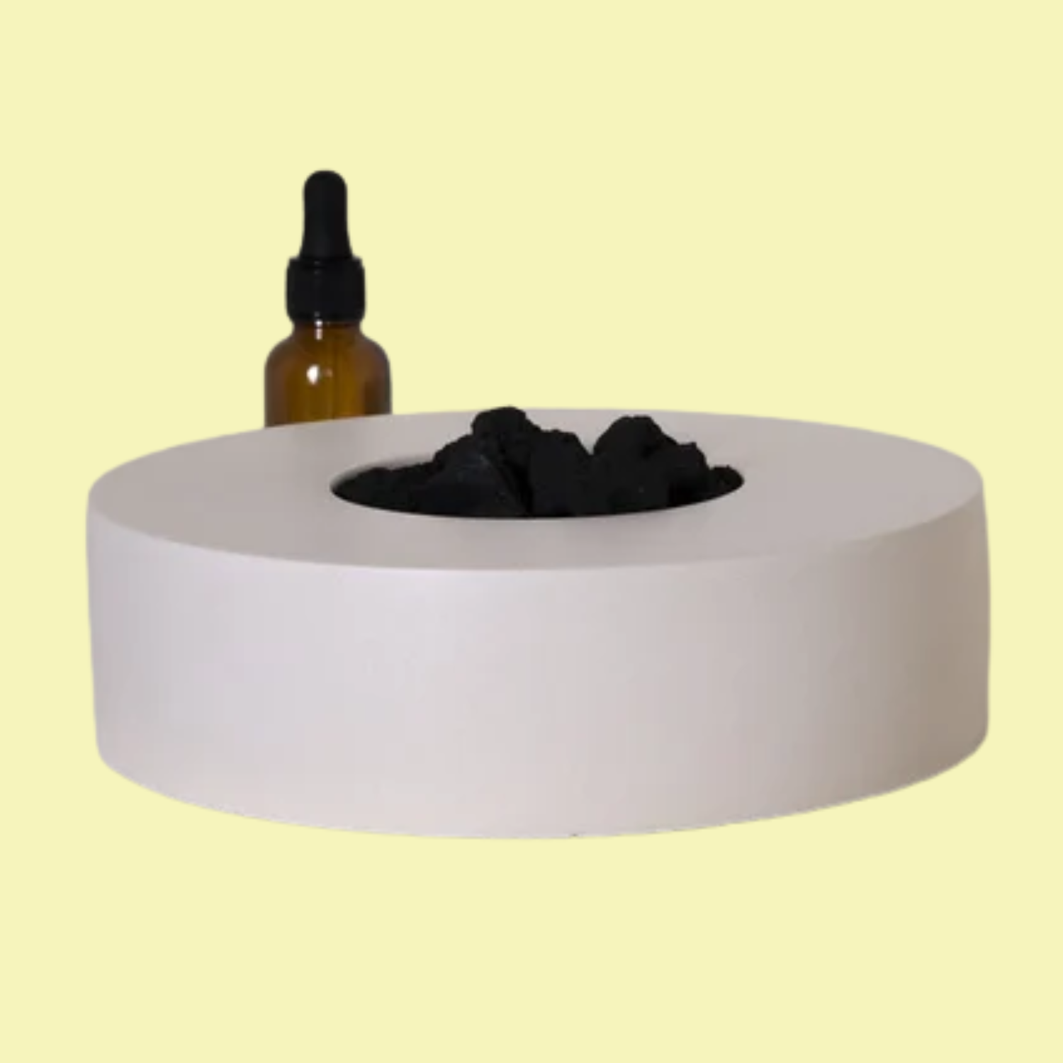 A white circular bowl with black lava rocks and a bottle of essential oil with a dropper