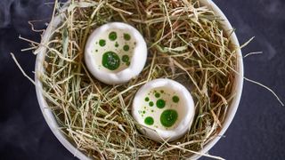 Egg, bacon and maitake mushrooms served in egg-shaped cups on a nest of hay