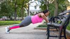 A woman performing a push-up on a park bench