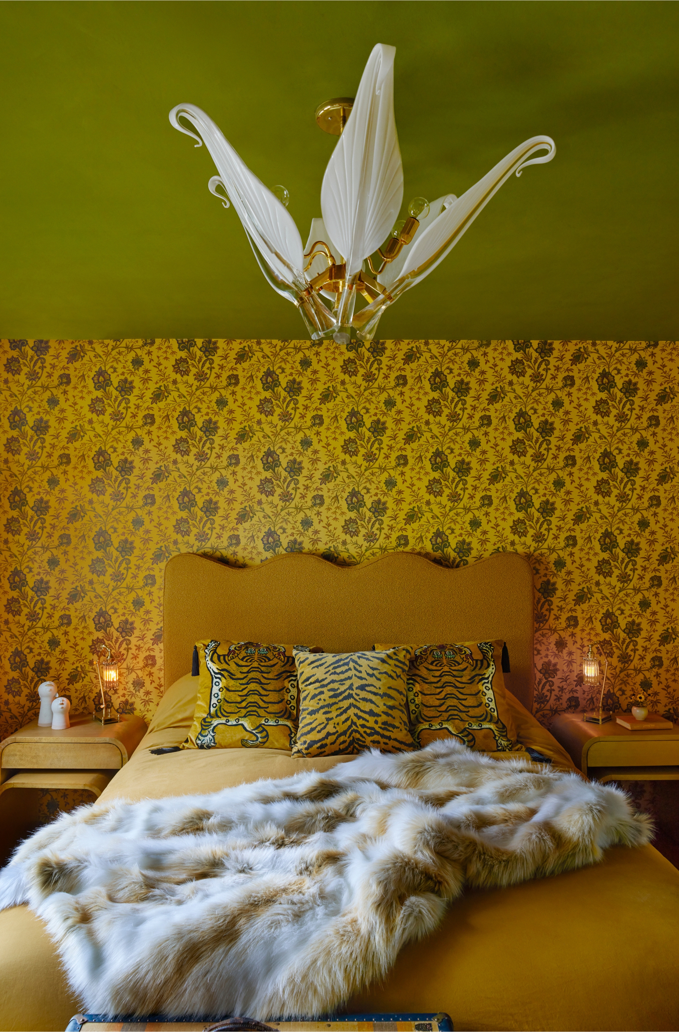 a yellow and green bedroom with a gold bed head and tiger print cushions, a decorative glass light is over the bed