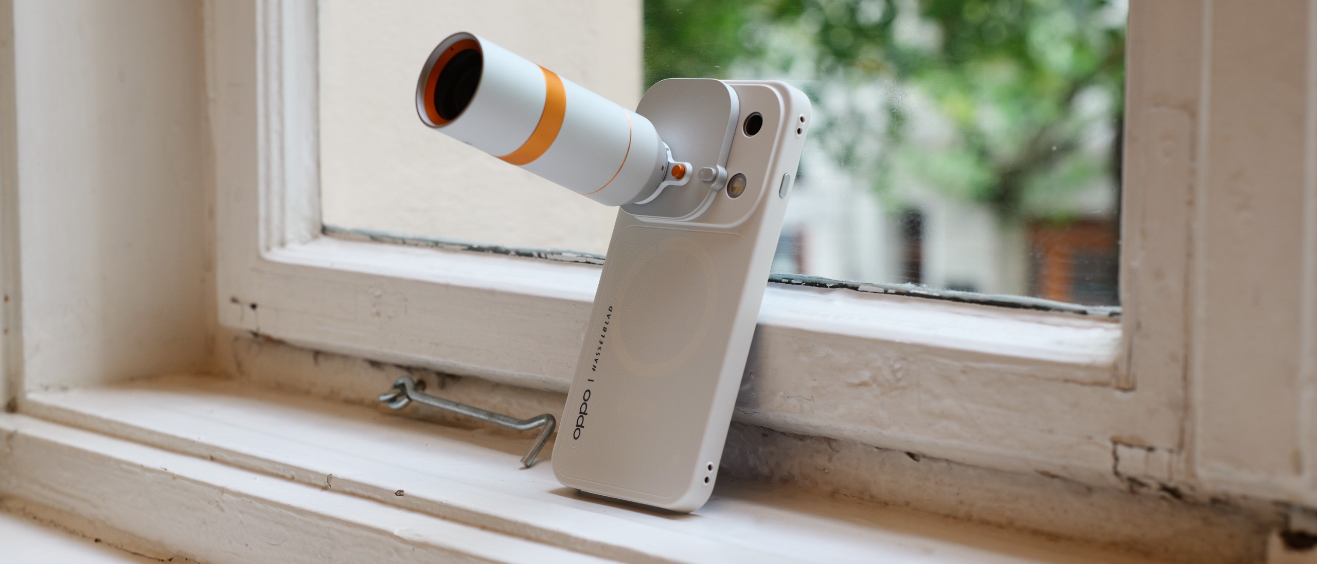 White Oppo Find X10 Pro Max standing on a windowsill with a long white-and-orange telephoto lens accessory attached.