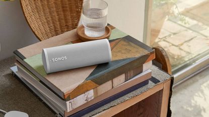 Sonos Roam in white resting on pile of books on side table