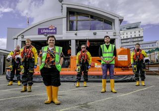 Susan stands outside a lifeboat station in Southend - wearing a hi-vis jacket and sturdy boots - with several of the station's volunteer crew