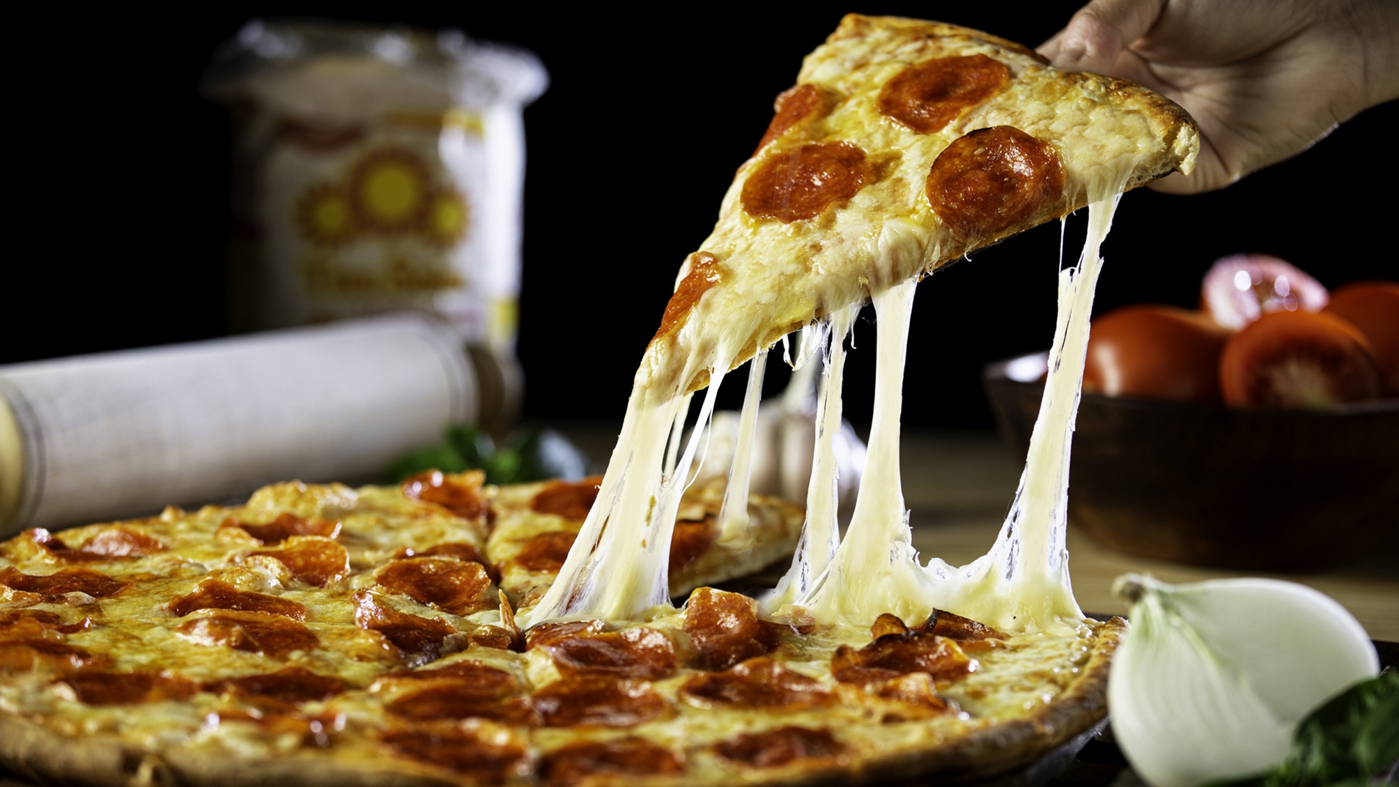 A pepperoni pizza with a hand getting a cheesy slice.
