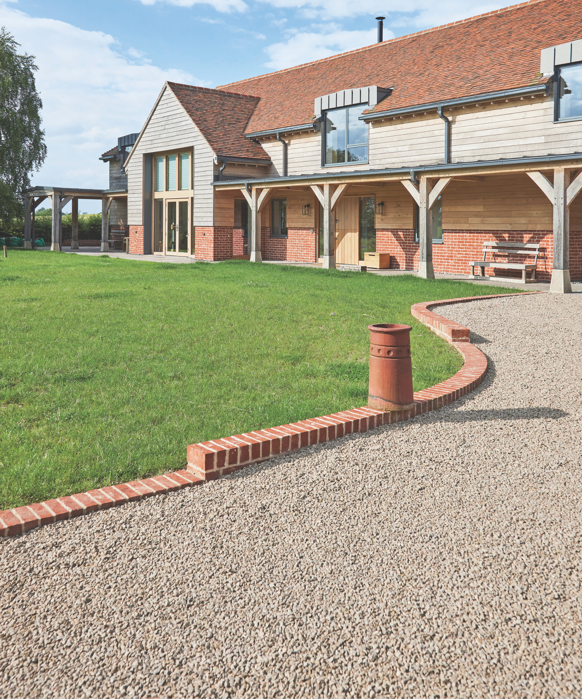 Gravel driveway with a brick line in between it and the lawn with a house behind it