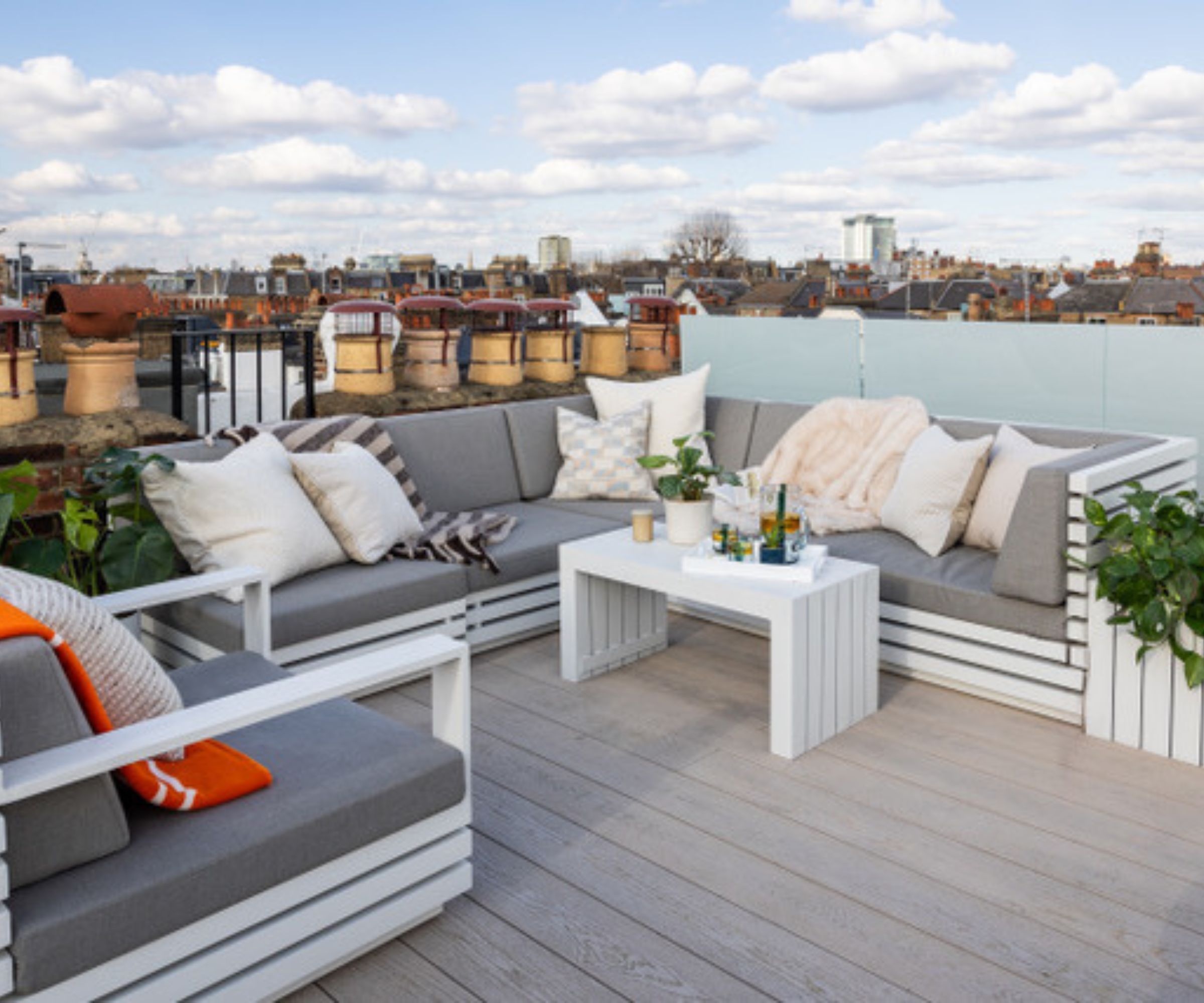 Grey corner sofa with cushions and throws, white coffee table, rooftop deck overlooking London chimney pots.