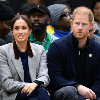 Meghan Markle wears a gray blazer and sits next to Prince Harry, who has balding red hair