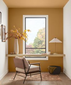 modern home office with dark yellow accent wall and ceiling, two white walls, desk in front of window with neutral armchair 