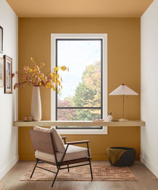 modern home office with dark yellow accent wall and ceiling, two white walls, desk in front of window with neutral armchair