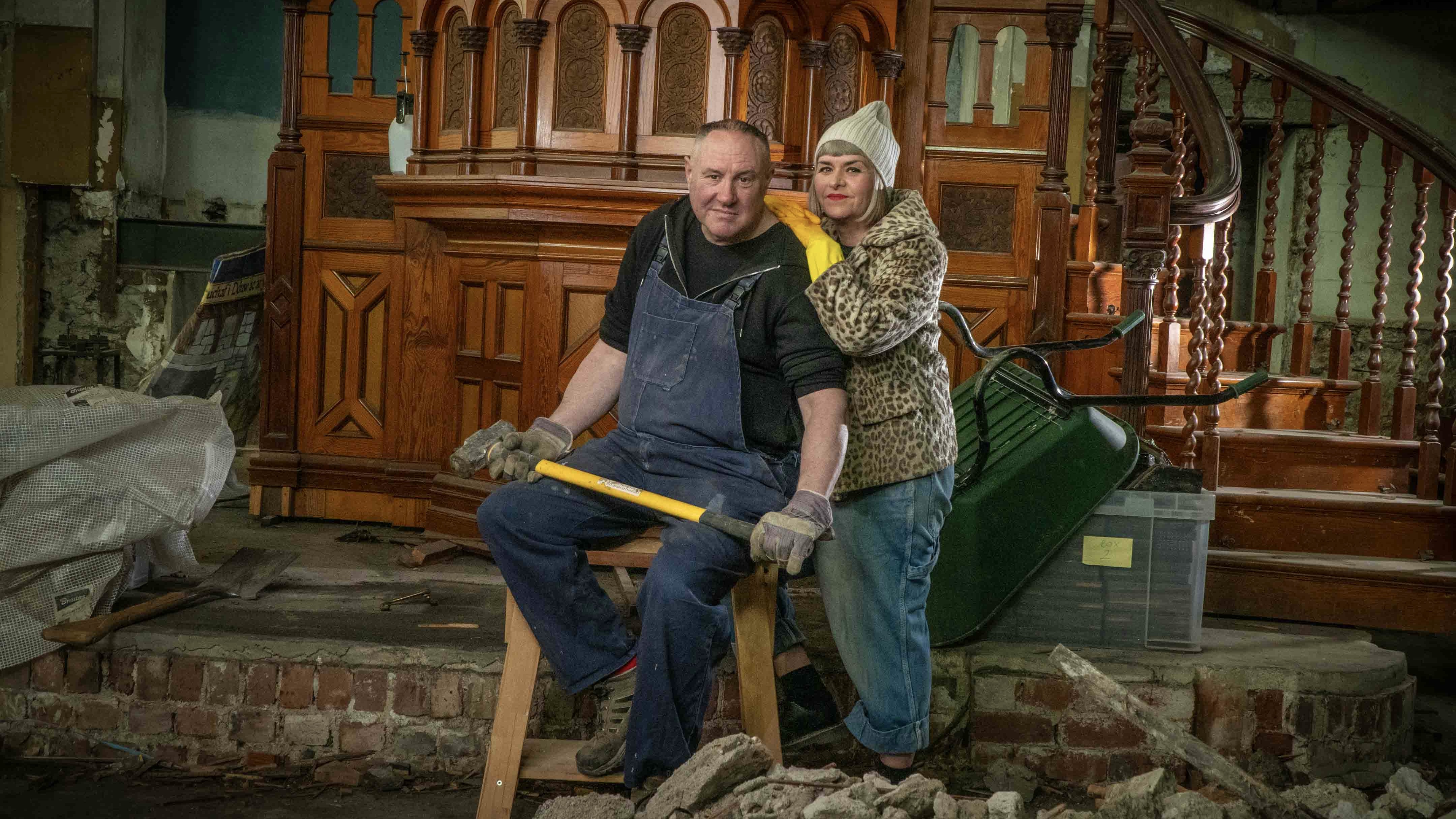Keith Brymer Jones seated holding a hammer and Marj Hogarth standing in front of the pulpit amid rubble in Our Welsh Chapel Dream
