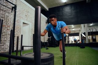 A young black man performs a sled push exercise in a gym.