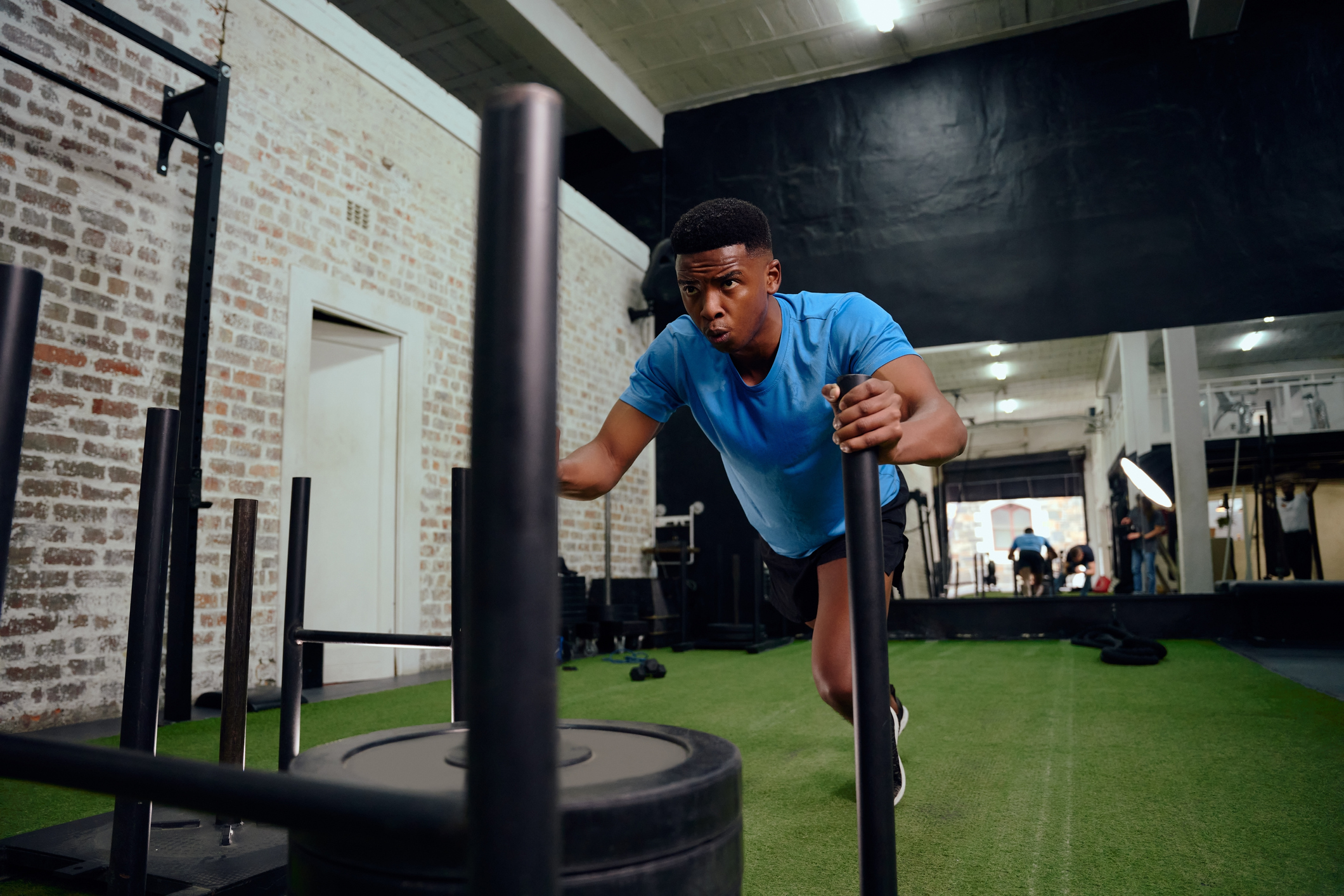A young black man is doing a sled push exercise at the gym.